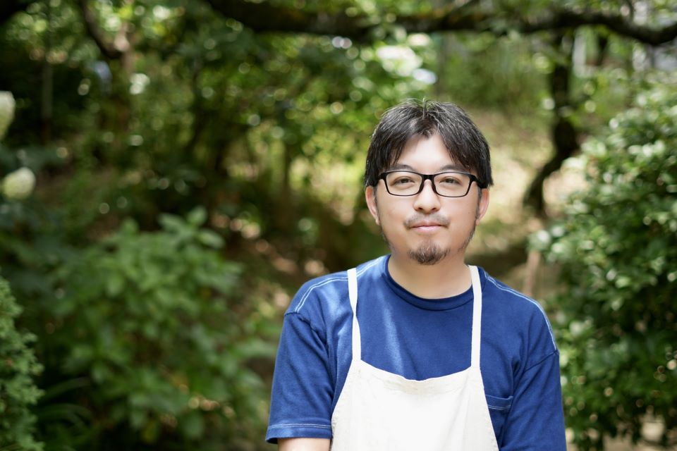 【写真】高野賢二さんの上半身ポートレート。藍色のTシャツに白いエプロンを着ている。